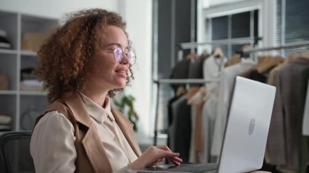 Vendas on-line, jovem gerente do sexo feminino sorridente com óculos organiza entrega para clientes em uma loja de internet com uma colega em uma loja de roupas — Vídeo de Stock