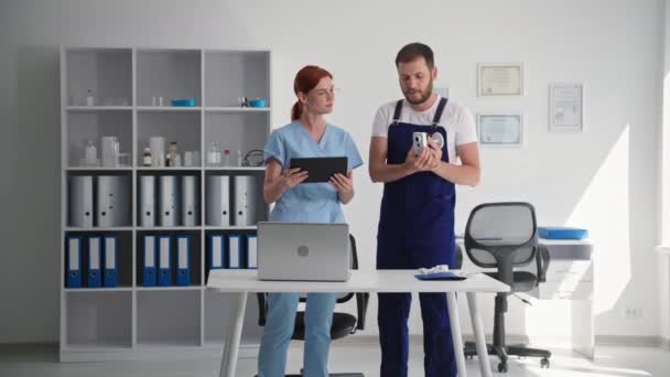 Moderní technologie, mladý muž vysvětluje ženě v lékařských šatech práci videokamery a ukazuje třídu, když stojí v kanceláři kliniky — Stock video