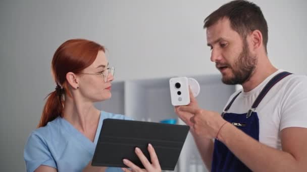 Відеоспостереження, молодий чоловік і жінка-лікар обговорюють встановлення прихованої камери спостереження в клінічному кабінеті — стокове відео
