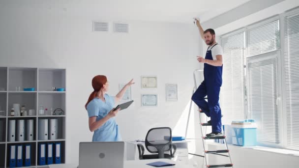 Installation av övervakningskamera på kontor, unga kvinnliga läkare kontrollerar videolänk med CCTV-kamera under installationen av manliga säkerhetsspecialister på arbetsplatsen — Stockvideo