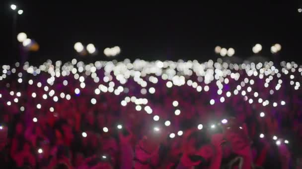 Невпізнавана група фанатів, що тримають мобільні телефони з ліхтариками в руках в нічний час, атмосфера концерту поза фокусом — стокове відео