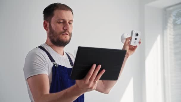 Kamera zur Aufzeichnung von Überwachungsvideos, Porträt eines jungen Mannes in Uniform, der die Kamera mit einem Tablet für die Installation in Innenräumen überprüft — Stockvideo