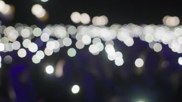 Розмитий фон, багато ліхтарів в руках натовпу людей під час нічного концерту на відкритому повітрі — стокове відео