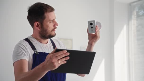 Retrato de oficial de segurança do sexo masculino feliz verificando uma câmera de vigilância escondida através de um aplicativo em tablet, sorrindo e olhando para a câmera — Vídeo de Stock