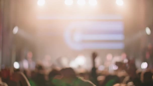 Рок-гурт виступає на концерті вночі, силуети фанатів піднімають руки перед яскравими барвистими стробними вогнями на сцені — стокове відео