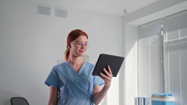 Salle de sécurité, jeune femme portant des lunettes vérifie le fonctionnement de la caméra de surveillance sans fil à l'aide d'une application sur tablette numérique, montre la classe et regarde la caméra — Video