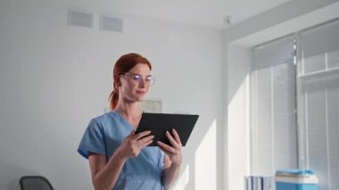 Gizli güvenlik kamerası, gözlüklü kadın doktor dijital tablet üzerindeki bir uygulamayı kullanarak kablosuz güvenlik kamerasını kontrol ediyor, sınıfını gösteriyor ve kameraya bakıyor.