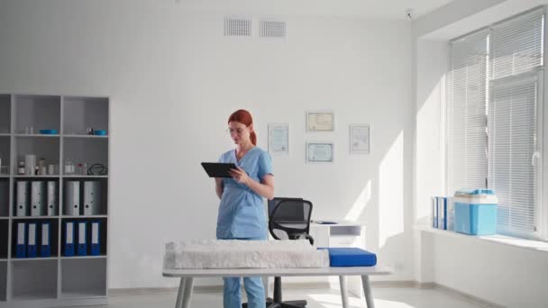 Κάμερα του συστήματος ασφαλείας, νεαρή γυναίκα με ψηφιακό tablet στα χέρια της παρατηρεί δωμάτιο με βιντεοκάμερα και μια εφαρμογή στο tablet, ενώ στέκεται στο χώρο εργασίας — Αρχείο Βίντεο