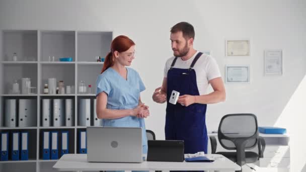 Caméra de vidéosurveillance de haute technologie, employé masculin racontant à la jeune femme le fonctionnement de la caméra de surveillance cachée et de l'application sur ordinateur portable et tablette numérique tout en restant debout dans son bureau — Video