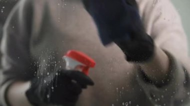 Evde temizlik ve dezenfekte işlemi, koruyucu eldivenli bir kız cama serpiştirir ve paçavra ile ovuşturur, kadın eli baş parmağını kaldırır.