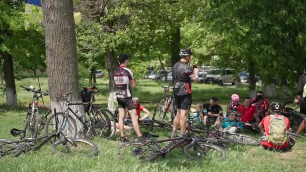 Kherson, Ucrânia 10 de agosto de 2021: descanso ativo, grupo de jovens em sportswear em capacetes com bicicletas estão descansando no prado verde entre as árvores — Vídeo de Stock