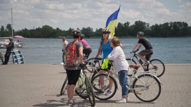 Херсон, Украина 10 августа 2021 года: молодые женщины, ведущие активный образ жизни, общаются, стоя на велосипеде на фоне неба и реки после прогулки по городу — стоковое видео