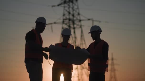 Werkteam van ingenieurs met project in hun handen bespreken de bouw van nieuwe stroomnet achtergrond van toren en zonsondergang, silhouet — Stockvideo