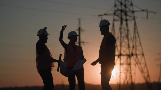 Successful work of engineers, happy young male and female specialists rejoice at completed project of power grid background of power tower and sunset, silhouette — Stock Video