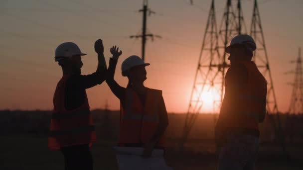 Projet réussi de réseau électrique, équipe d'ingénieurs professionnels se donnent cinq et se réjouissent de la construction d'une nouvelle tour haute tension au coucher du soleil, silhouette — Video