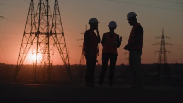 Elektrik tesisatı ve tedariği, profesyonel elektrik mühendisi gün batımının arka planında ağaç kuleleri inşa etmeyi tartışıyor, siluet — Stok video