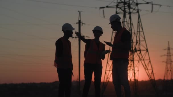 Succesvolle ingenieurs, mannen en vrouwen bespreken een project voor de bouw van een elektriciteitscentrale en een elektrische lijn om de stad of het dorp van elektriciteit te voorzien, hun beschermhelm af te doen en deze op te tillen; — Stockvideo