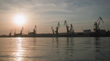 Konteynır yüklemek için vinçleri ve kargo gemilerine tahılları olan şehir ticaret limanı. Nehirden gün batımı manzarası, siluet.