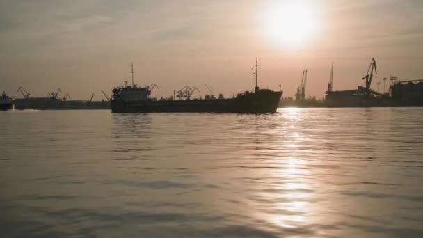 Transport maritime, cargo pour le trafic et les conteneurs arrive au port fluvial dans la partie industrielle de la ville avec des grues au coucher du soleil, vue de l'eau — Video
