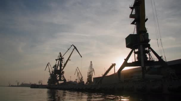 Flusshafen für den internationalen Handel und Frachttransport von Containern und Getreide auf Seeschiffen mit Frachtkränen am kommerziellen Steg vor dem Hintergrund des Sonnenuntergangs und des glänzenden Wassers, Silhouette — Stockvideo