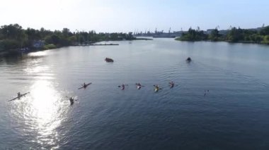 KHERSON, UKRAINE - 20 Eylül 2021, kürek çeken, ellerinde kürekleri olan bir grup insan rıhtım ve güneş ışınları, siluet nehrinde kürek çekiyorlar.