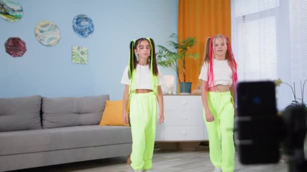 Niños bloggers bailan música en casa delante del teléfono móvil, novias filman videos para redes sociales y muestran los pulgares hacia arriba — Vídeo de stock