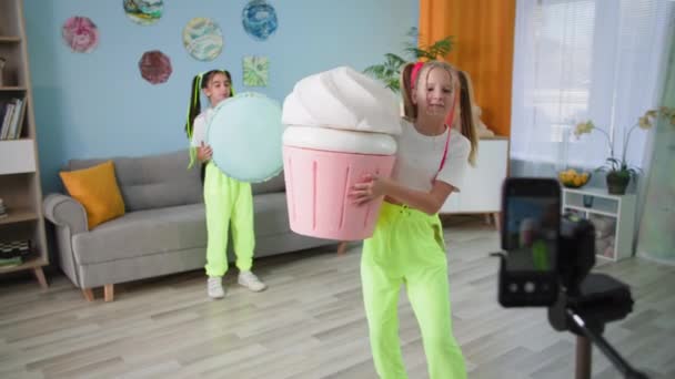 Doce diversão, namoradas se divertir na frente da câmera do telefone móvel com grandes figuras de gesso sorvete e macaroon, crianças atirar histórias em casa — Vídeo de Stock