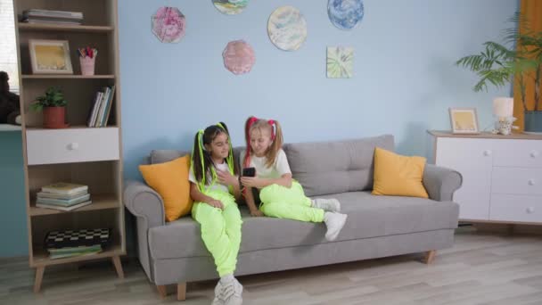 Children entertainment, trendy friends on sofa share video to social media, little girls use mobile phone at home — Stock Video