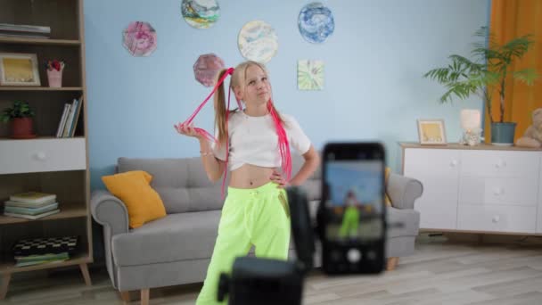 カラフルなピグテールを持つスタイリッシュな女の子は自宅で携帯電話でビデオを記録し、ブロガーの子供は、インターネットのための新しい傾向を撮影 — ストック動画