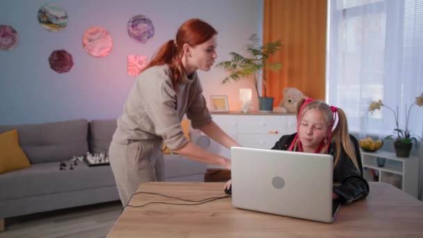 Problemen van ouderschap in het gezin, vrouw scolds een dochter voor videospelletjes thuis, klein meisje uitdagend beantwoordt haar moeder en glimlacht zitten aan de tafel — Stockvideo