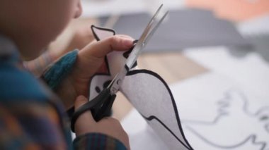 Cadılar bayramı kutlaması sırasında ev dekorasyonu, çocuk hobisi ve yaratıcılığı için makasla kağıt üzerinde hayalet şekline bürünmüş küçük çocuk ellerine yakın plan.