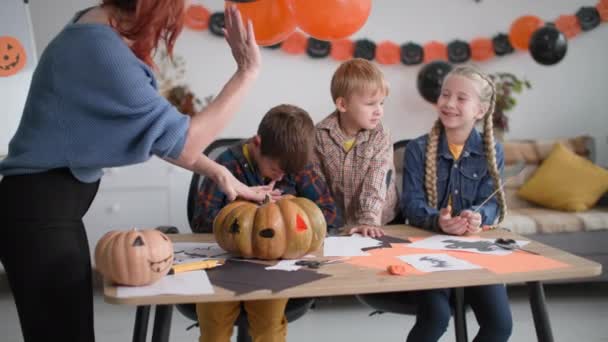 Halloween para los niños lindos en casa, la madre da pequeño hijo cinco y ayuda a hacer decoraciones para las vacaciones en el fondo de guirnaldas en forma de calabazas — Vídeos de Stock
