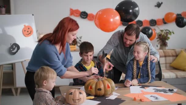 Familj av 5 förbereder sig för Halloween hemma, föräldrar hjälper barn att göra dekorationer med pumpor på bakgrund av ballonger och girlanger — Stockvideo