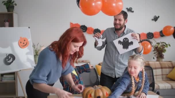 Sonbahar tatili, çocuklarla mutlu bir aile cadılar bayramı hazırlığı sırasında hayaletlerin figürleriyle çelenk ve balonlarla süslemelerin arka planına karşı oynuyorlar. — Stok video