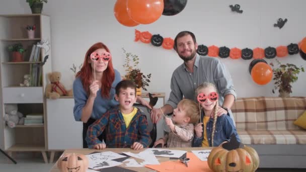 Halloweenfest, glad familj poserar på kamera med masker i form av pumpor och hatt på pinne och sedan säger Boo — Stockvideo