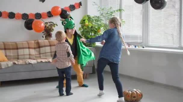 Festa de Halloween, menino em traje de dragão corre com amigos em uma sala decorada com abóboras, guirlandas e balões — Vídeo de Stock