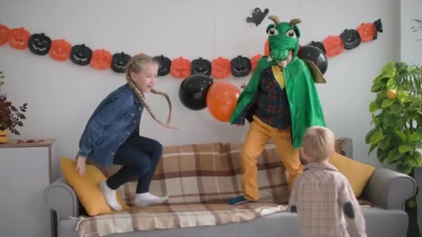 Drie vrienden spelen inhaalslag in de kamer, jongens en meisje rennen rond het huis met decoraties voor vakantie Halloween — Stockvideo