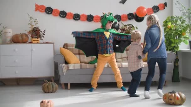 Infanzia felice, i bambini scappano da un ragazzo in costume da drago, gli amici si divertono insieme a casa durante la celebrazione di Halloween — Video Stock