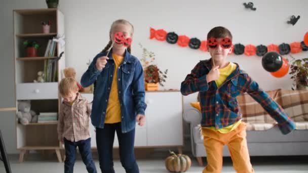 Niños se divierten bailando con máscaras en forma de calabazas en el fondo de guirnaldas y globos en casa, feliz halloween — Vídeo de stock