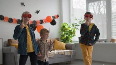 Sonbahar tatili, arkadaşlar balkabağı şeklinde maskelerle ve evde balon ve çelenk arka planında şapkayla dans ederken eğleniyorlar.
