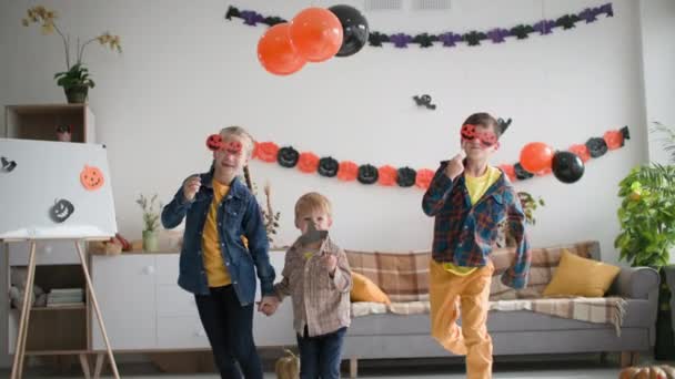 Casa halloween, amigos se divertir dançando com máscaras na forma de abóboras e chapéu no fundo de guirlandas e balões — Vídeo de Stock