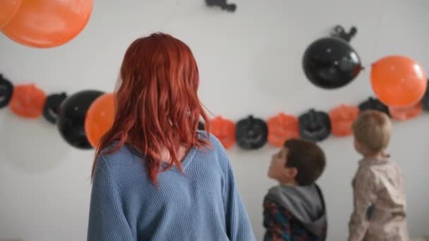 Portret van mam, gelukkig jong vrouw kijkt naar de camera en glimlacht op de achtergrond van kinderen spelen met ballonnen, Halloween sfeer — Stockvideo