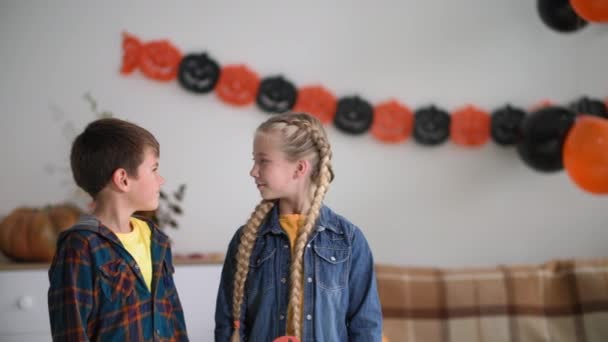 Ritratto di bambini mostrano il segno di approvazione, amici con maschere di Halloween in forma di zucche posare a casa sullo sfondo di ghirlande e decorazioni autunnali, macchina fotografica in movimento — Video Stock