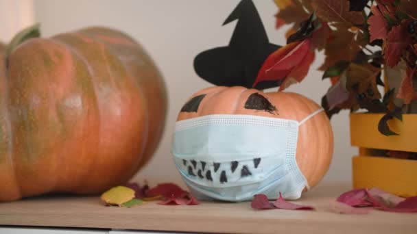 Halloween decoratie, pompoen met hoed en beschermende medische masker op gezicht staat op tafel met herfstbladeren, coronavirus en quarantaine — Stockvideo