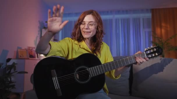 Lehrerin leitet Online-Gitarrenunterricht mit Laptop und sitzt abends auf Couch im Zimmer — Stockvideo