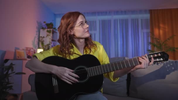 L nauczyciel daje lekcje gry na gitarze instrumentalnej za pomocą komunikacji wideo na laptopie podczas siedzenia na kanapie wieczorem — Wideo stockowe
