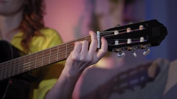 Woman with glasses loves music and enjoys playing instrumental guitar, smoothing her hands on musical instrument smiling and looking at camera — Stockvideo