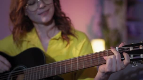 Meisje met liefde in haar hart speelt gitaar en geniet van muziek terwijl ontspannen thuis in de avond, glimlachen en kijken naar de camera — Stockvideo