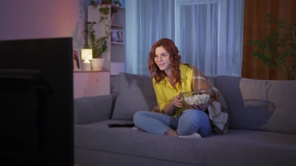 Charming girl resting at home eating popcorn and watching sports match on TV clapping hands on leg with excitement and joy — Video Stock