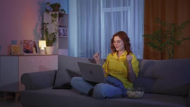 Beautiful woman reacts emotionally while watching sports matches or playing in online casino on laptop while sitting on couch at home in evening — Vídeo de Stock